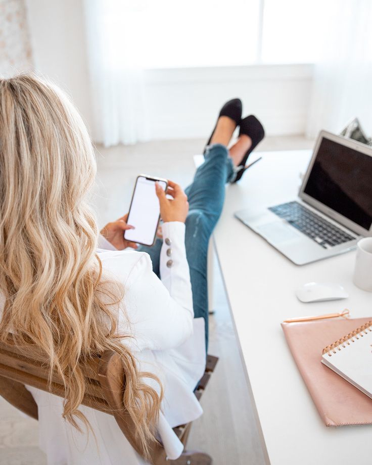 A woman relaxing at her desk with her feet up, scrolling her phone