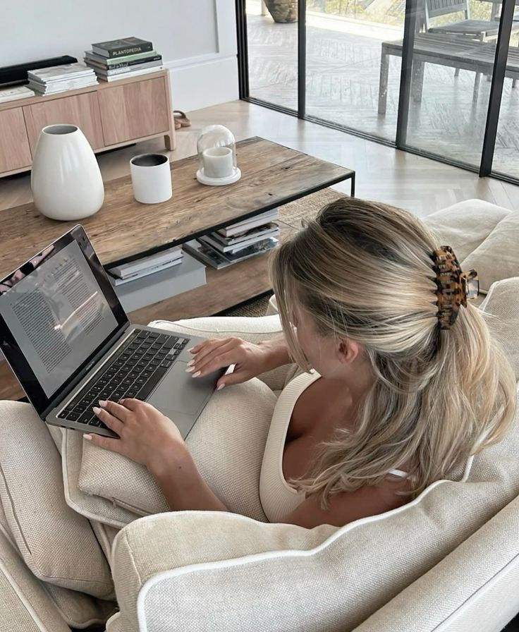 A woman working on a laptop from a bright living room couch
